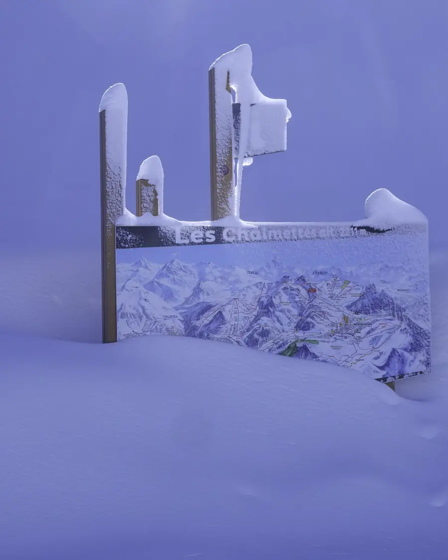 Panneau d’orientation des pistes à demi enseveli sous la neige, dans la lumière bleue du crépuscule